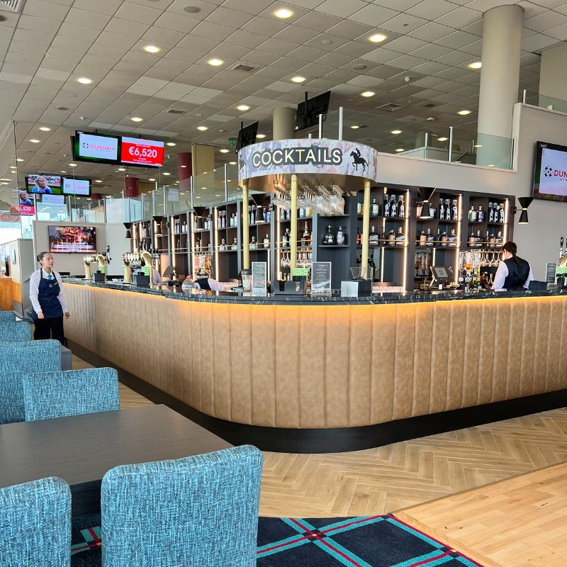 The Saddle Cocktail Bar: a long curved bar with shelves of bottles.