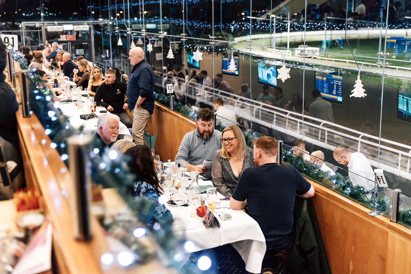 Christmas party tables beside the glass, the floodlit track outside.